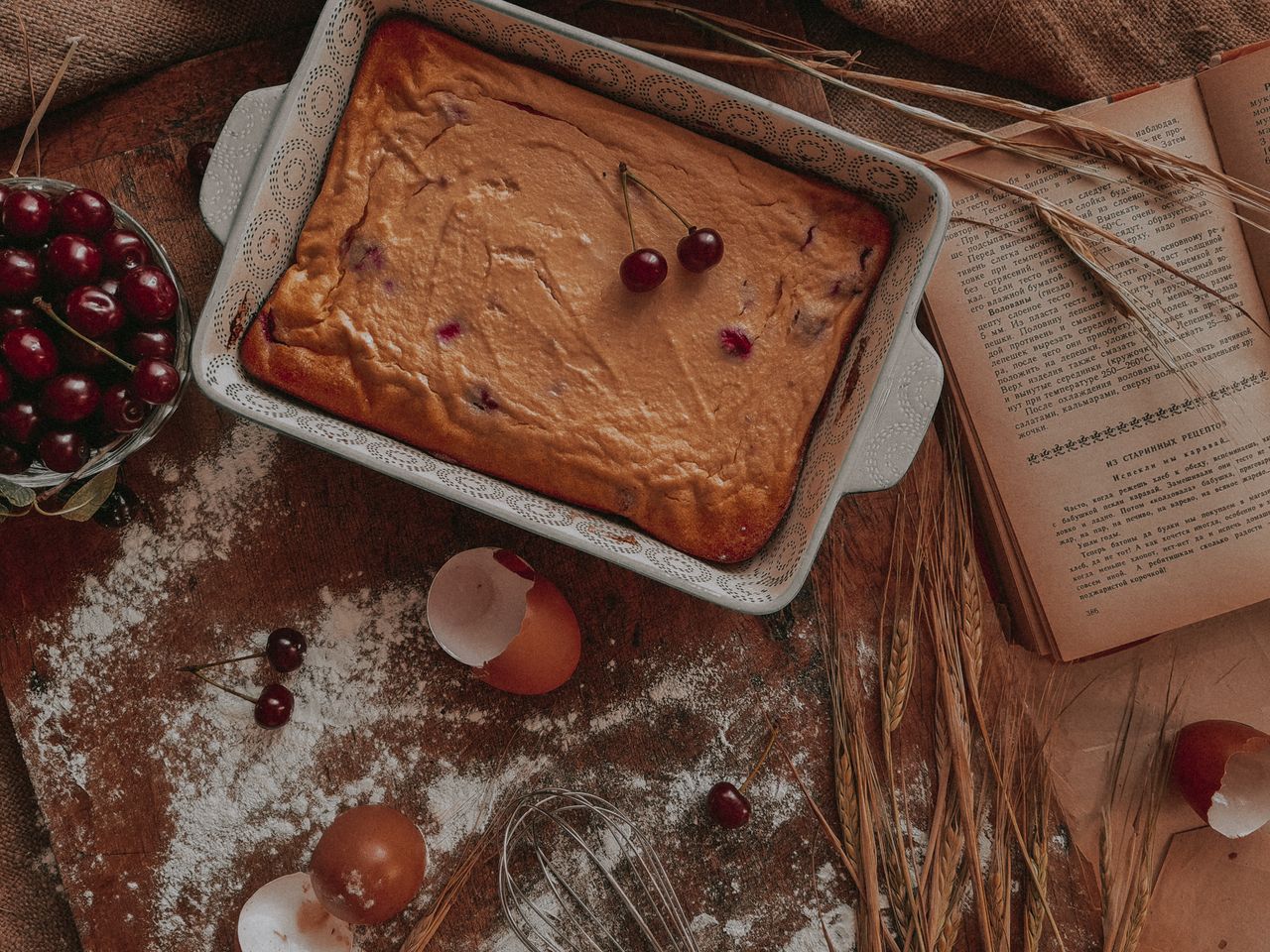 Delicious cherry cake in a rustic setting with eggshells, flour, and open cookbook for baking inspiration.