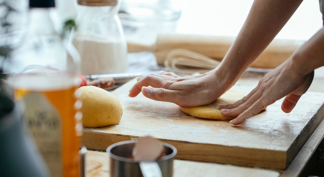 Female hands kneading fresh dough on wooden chopping board with flour in kitchen